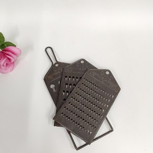 May include: A vintage 3-in-1 Lightning Grater with a metal frame. The grater has three different sized holes for grating different types of food.