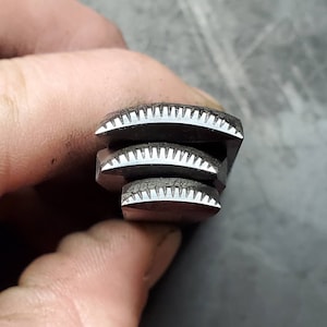 May include: Close-up of three stacked, dark metal objects with a semi-circular shape. Each object has a series of small, evenly spaced teeth along the curved edge. The objects are stacked on top of each other, with the smallest at the bottom.