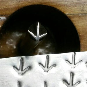 May include: A metal stamp with bird footprints and bird silhouettes. The stamp is silver and has a rectangular shape with a hole on the left side. The bird footprints are arranged in rows, and the bird silhouettes are on the right.