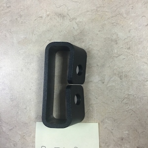 May include: A black plastic belt loop with two holes. The text "BELT LOOP" is written on a yellow sticky note below the loop.