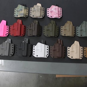 May include: A collection of 17 different coloured holsters for concealed carry. The holsters are made of a durable material and have a variety of colours and patterns.