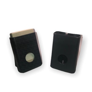 May include: Two black cases for a small electronic device. One case has a textured pattern and a circular cutout. The other case is plain black with a circular cutout.