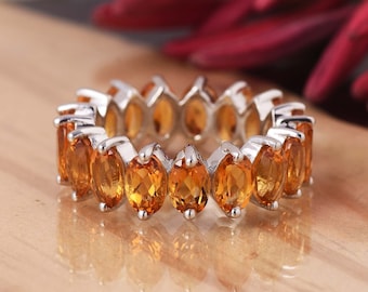 May include: A silver band ring with a row of oval-shaped orange gemstones. The ring is on a wooden surface.