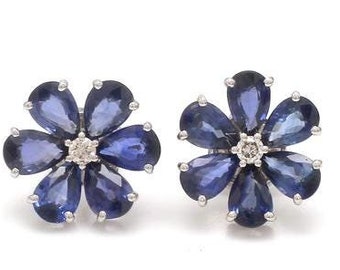 Puede incluir: Un par de pendientes de plata en forma de flor con piedras de zafiro azul y un pequeño diamante en el centro de cada flor.