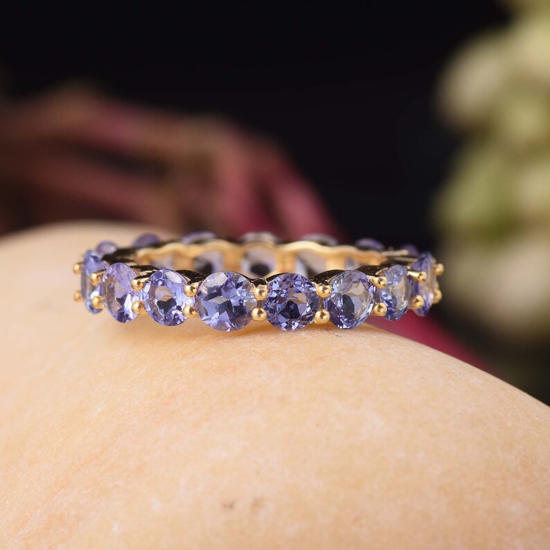 May include: A gold band ring with a row of round, purple gemstones.