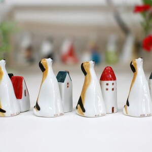 May include: A set of eight ceramic figurines, each depicting a dog with a house on its back. The houses are painted in various colors, including red, blue, and green. The dogs are all looking up, and their tails are wagging.