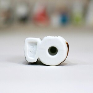 May include: White ceramic figurine of a number 8 with brown accents. The figurine has a hole in the center and the bottom is marked with the number "2147".