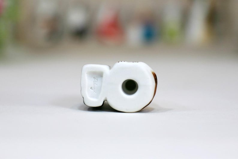 May include: White ceramic figurine of a number 8 with brown accents. The figurine has a hole in the center and the bottom is marked with the number "2147".