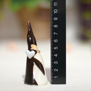 May include: A ceramic penguin figurine holding a white heart. The penguin is black and white with a gold ring around its neck. The figurine is approximately 5 inches tall.