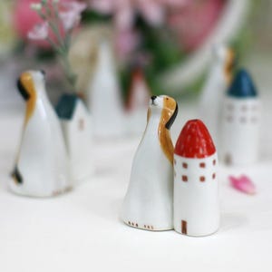 May include: A set of ceramic figurines depicting a dog and a house with a red roof. The figurines are painted in white, brown, red, and blue.