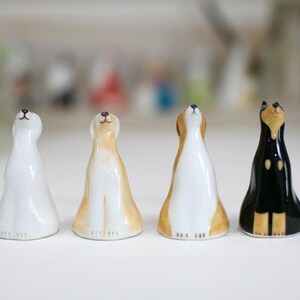 May include: Four ceramic figurines of dogs, each with a different color and design. The dogs are all looking up, and they are standing on a white surface.