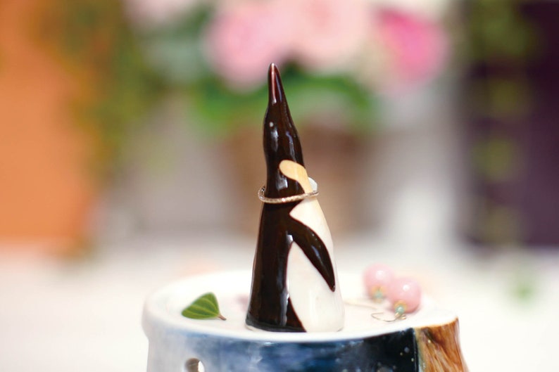 May include: A ceramic penguin ring holder with a black and white design. The penguin is holding a gold ring. The ring holder is sitting on a white and blue ceramic base.
