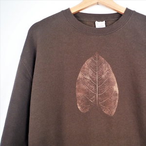 May include: A brown sweatshirt with a leaf print in the centre.