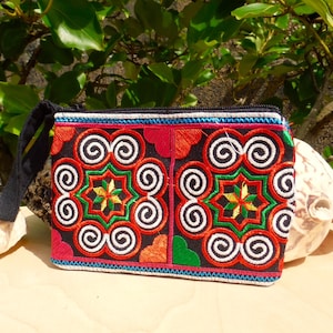 Puede incluir: Una pequeña bolsa negra con cremallera con un diseño bordado de colores. El diseño presenta espirales y estrellas rojas, naranjas, verdes, amarillas y blancas sobre un fondo negro.