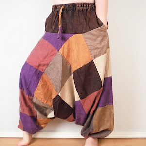 Könnte beinhalten: Weit geschnittene Hose mit einem Patchwork-Design aus quadratischen Stoffbahnen in den Farben Violett, Braun, Orange und Creme. Das Kleidungsstück hat einen dunkelbraunen elastischen Bund mit passendem Kordelzug und einen tiefen Schritt.