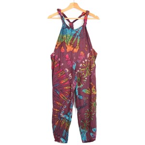 May include: Tie-dye overalls with a purple base and colorful swirls. The straps are tied at the back of the neck.