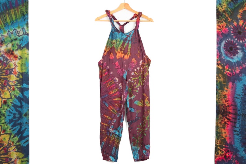 May include: Tie-dye overalls with a purple base and colorful swirls. The straps are tied at the back of the neck.