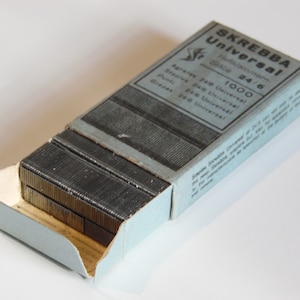 Puede incluir: Una caja azul de 1000 grapas con la etiqueta "SKREBBA Universal" con el texto "Heftklammern Stabe 24/6" y "Agrates 24/6 Universal, Staples 24/6 Universal, Punti 24/6 Universal, Grepes 24/6 Universal".