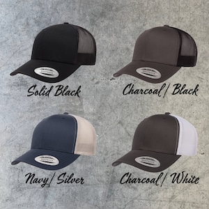 May include: Four trucker hats in different color combinations. The hats are black, charcoal with black mesh, navy with silver mesh, and charcoal with white mesh. Each hat has a Snapback closure and the word "SNAPBACK" is printed on the back of the hat.