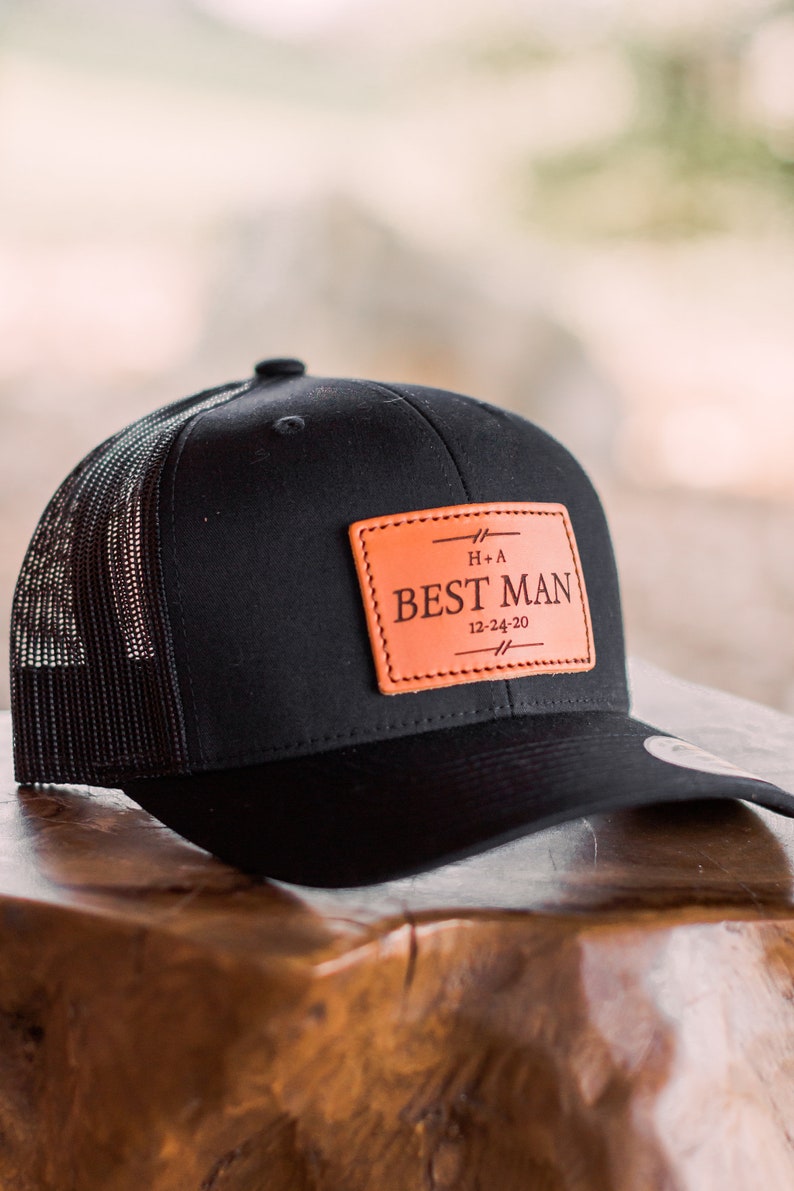 May include: Black and brown trucker hat with a leather patch that says "Best Man" with the date "12-24-20" and the initials "H+A".