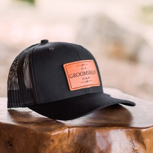 May include: Black trucker hat with a brown leather patch that says "It's a Groomman 12.14.20".