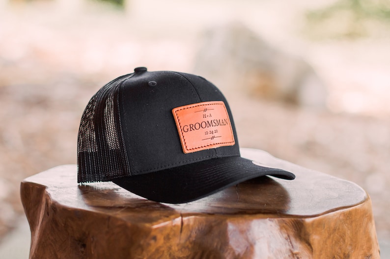 May include: Black trucker hat with a brown leather patch that says "It's a Groomman 12.14.20".