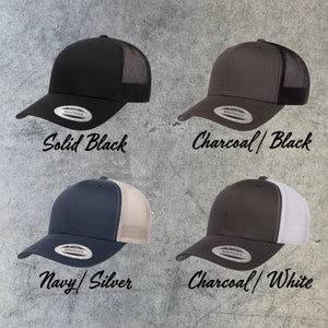 May include: Four trucker hats in different color combinations. The hats are black, charcoal with black mesh, navy with silver mesh, and charcoal with white mesh. Each hat has a Snapback closure and a label that says "SNAPBACK".