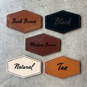 May include: Five leather hexagon-shaped tags with different colors and text. The colors are buck brown, black, medium brown, natural, and tan. The text on the tags reads "Buck Brown", "Black", "Medium Brown", "Natural", and "Tan".