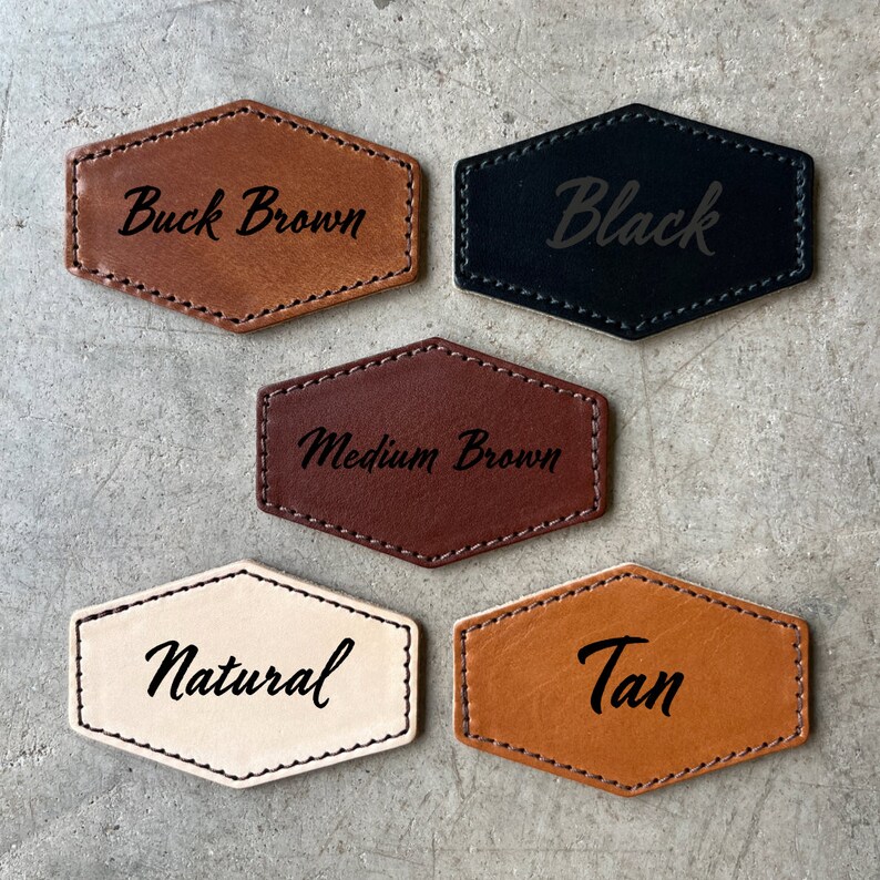 May include: Five leather hexagon-shaped tags with different colors and text. The colors are buck brown, black, medium brown, natural, and tan. The text on the tags reads "Buck Brown", "Black", "Medium Brown", "Natural", and "Tan".