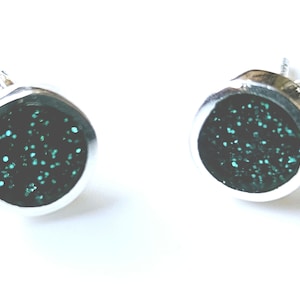 May include: A pair of silver stud earrings with a round, teal glitter design.