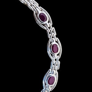 May include: A silver-toned metal bracelet featuring a series of interlocking rectangular links. The design includes three prominent oval-shaped, deep red cabochon stones, each securely set within a polished metal frame integrated into the chain.