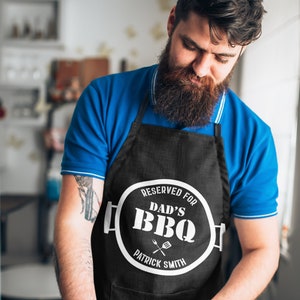 May include: Black apron with a white circle that says "Reserved for Dad's BBQ" with a grill and spatula graphic and the name "Patrick Smith" underneath.