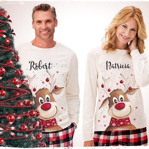 May include: Matching Christmas pajamas. The long-sleeved tops are cream-colored with a reindeer graphic and the names "Robert" and "Patricia". The bottoms are red and black plaid. A Christmas tree is on the left.