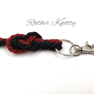 May include: A red and black braided rope keychain with a silver key ring and a silver clasp. The keychain is knotted in a decorative pattern. The text "Rather Knotty" is visible in the background.