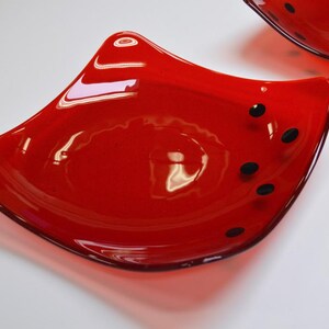 May include: Two red glass bowls with black dots. The bowls are shaped like a fish fin and have a glossy finish.