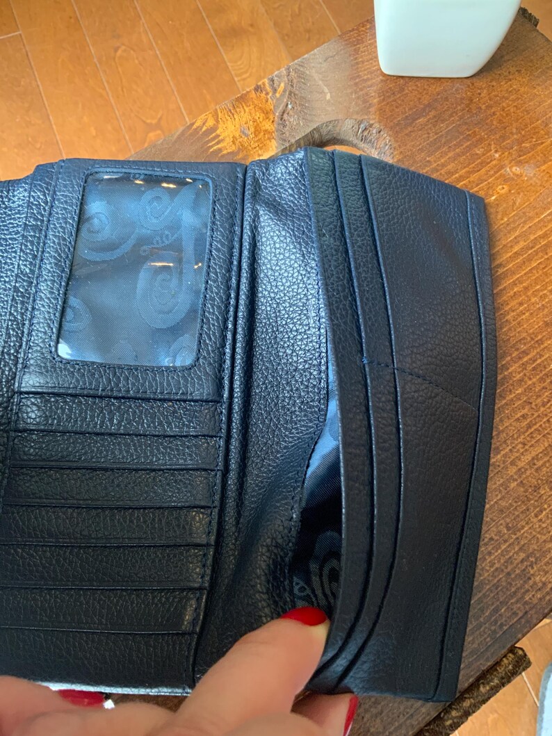 May include: Navy blue leather wallet, open to reveal card slots and a clear ID window. The wallet has a textured finish and a side pocket. The interior features a patterned fabric lining.