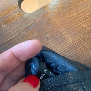 May include: Black leather glove with quilted stitching. The interior lining is a patterned blue fabric. The tag inside the glove reads "Made in China".