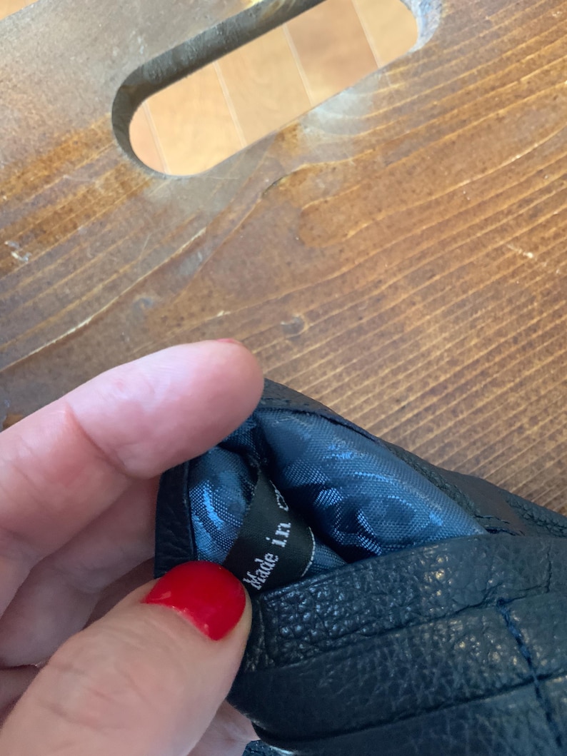 May include: Black leather glove with quilted stitching. The interior lining is a patterned blue fabric. The tag inside the glove reads "Made in China".
