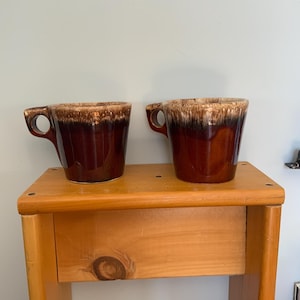 May include: A set of three ceramic mugs with a speckled, matte finish. The mugs are in shades of cream, light gray, and dark gray. Each mug has a simple, minimalist design and a rounded handle.