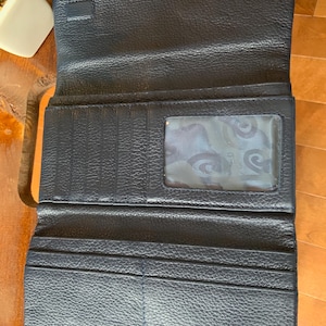 May include: Open navy blue leather wallet with multiple card slots and a clear ID window. The wallet is unfolded, revealing its interior compartments. The leather has a textured grain, and the wallet appears to be new.