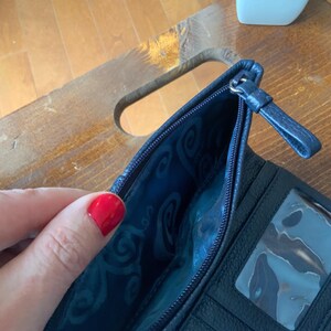 May include: Navy blue leather wallet with a zip. The interior has a patterned blue lining and a clear ID window. The wallet is open, showing the interior design.