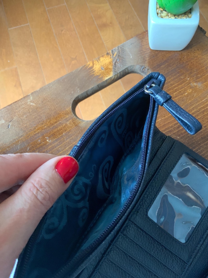 May include: Navy blue leather wallet with a zip. The interior has a patterned blue lining and a clear ID window. The wallet is open, showing the interior design.