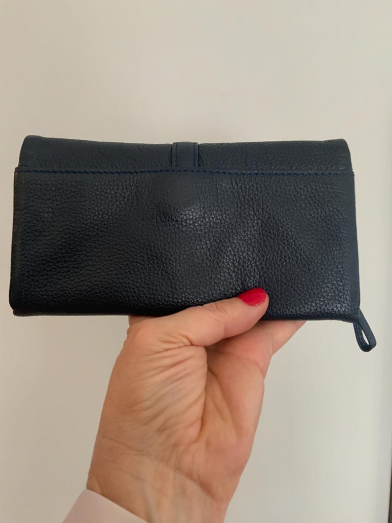 May include: A navy blue leather wallet with a textured finish. The rectangular wallet has a loop on the side. The wallet is held in a hand.