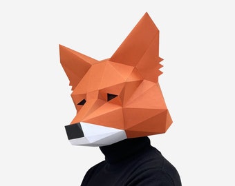 May include: A papercraft fox mask with orange and white details. The mask is made of folded paper and has a three-dimensional design.