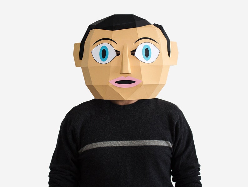 May include: A papercraft mask of a person's face with large blue eyes and a pink mouth. The mask is made of brown and white paper and has a black hair line.