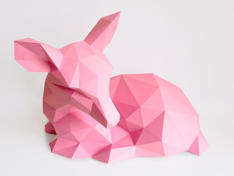 May include: A pink origami deer sculpture, made of paper, with a geometric design. The deer is lying down with its head turned to the side.