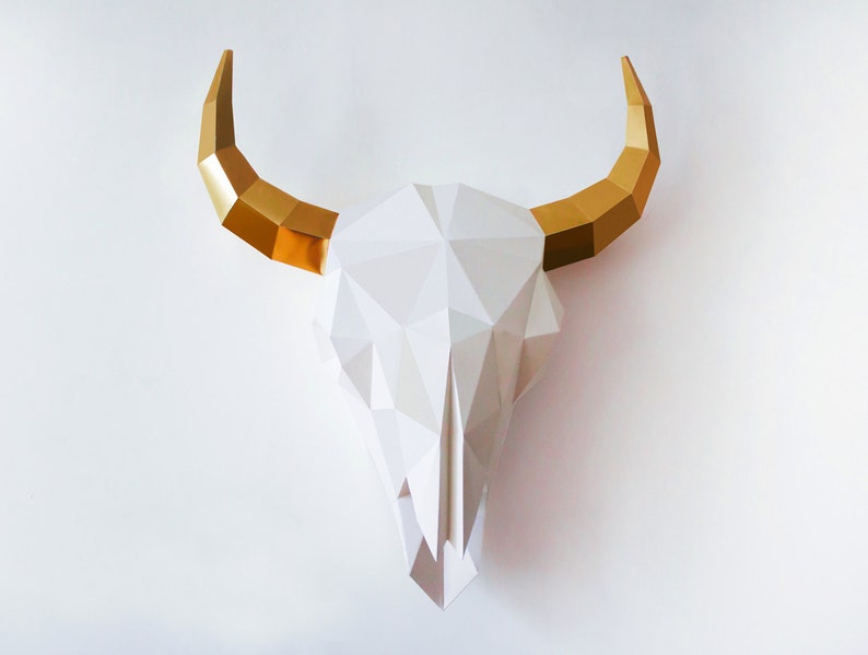 K&ouml;nnte beinhalten: Wei&szlig;er Papier-Stierkopf mit goldenen H&ouml;rnern. Der Sch&auml;del besteht aus gefaltetem Papier und hat ein geometrisches Design.