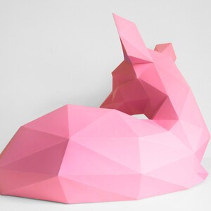 May include: A pink origami sculpture of a fox lying down. The sculpture is made of paper and has a geometric design.