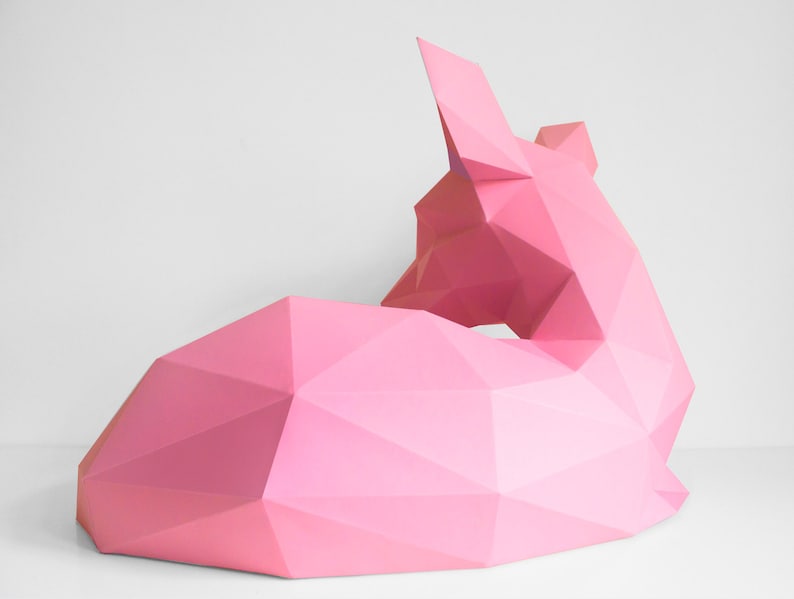 May include: A pink origami sculpture of a fox lying down. The sculpture is made of paper and has a geometric design.