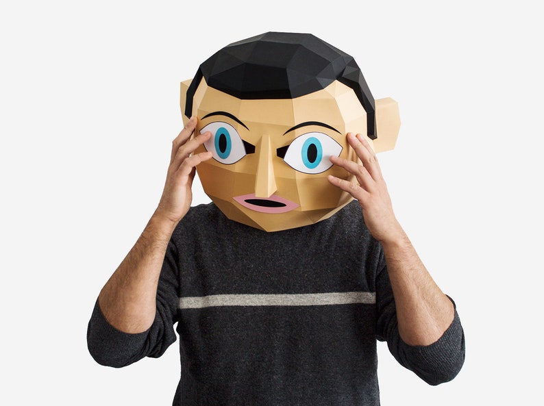 May include: A person wearing a paper mache mask with large blue eyes and a surprised expression. The mask is brown and beige with black hair. The person is wearing a gray sweater with a white stripe.